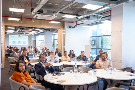 Photo of audience seated around round tables in a bright conference room.