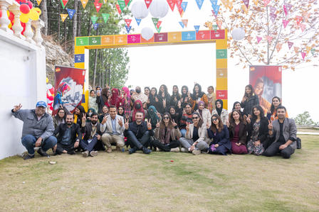 Group of people posing outdoors under a colorful arch with confetti and balloons.