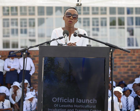 Speaker at podium with two microphones at official launch; crowd in white shirts behind.