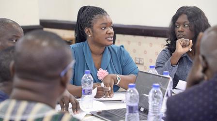 Blurred faces of people around a conference table with papers and water bottles.