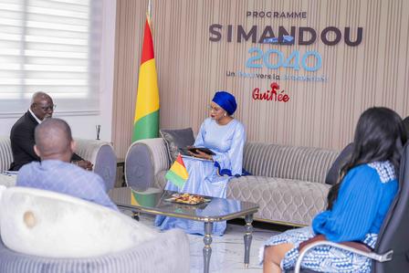 Officials seated around a glass table in a room with a Simandou 2040 banner.