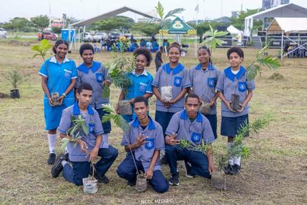 Group of volunteers in blue shirts posing with saplings at a tree-planting event.
