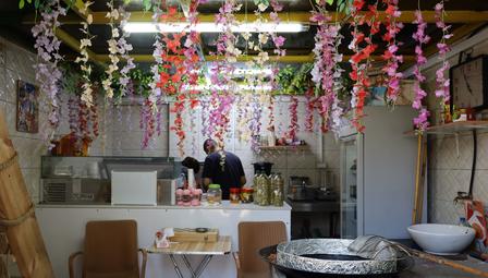 Cozy cafe interior with a wooden counter, hanging flower garlands, and customers in the background.