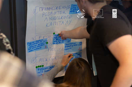 People gathered around a large board filled with blue handwritten notes and diagrams.