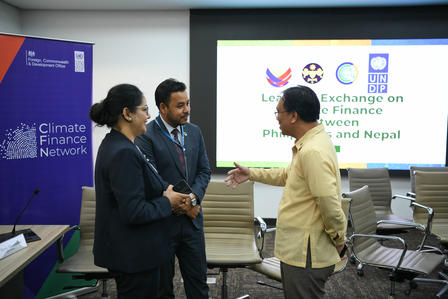 Photo: three men in a conference room shake hands before Climate Finance banners and a logo slide.
