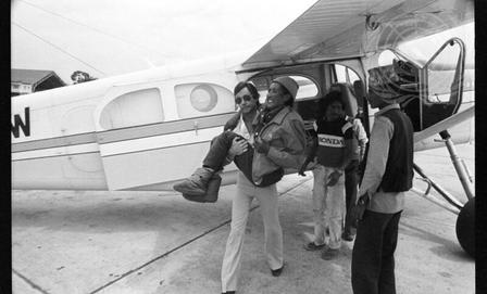 Black-and-white photograph of a small propeller plane with several people on the tarmac.