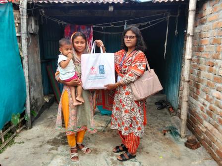 Two women with a baby stand outside a brick doorway; one holds a framed certificate.