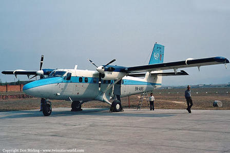 Photograph of a blue twin-engine high-wing airplane on a tarmac with two people nearby.
