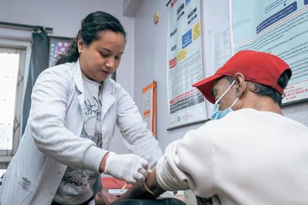 Healthcare worker in white coat and gloves examines patient wearing a red cap in clinic.