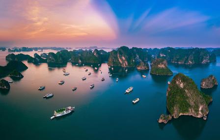 Aerial view of a tranquil bay with towering green limestone islets and boats at sunset.