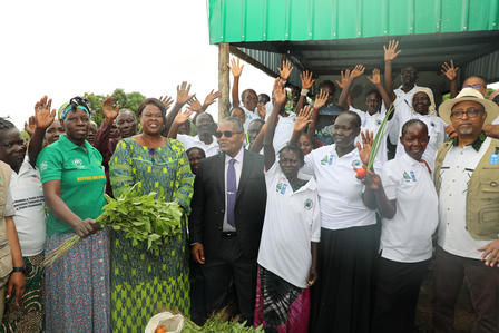 Outdoor group of people raising hands in celebration; some wear white shirts and green clothing.