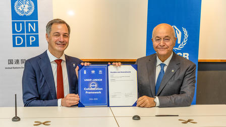 Two men in suits display a signed agreement in front of UNDP banners.