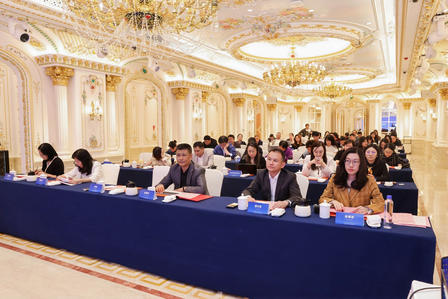 Formal conference in an ornate gold ballroom; attendees seated at blue-draped tables.