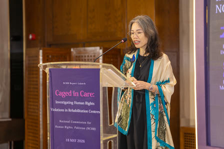 Female speaker at the podium wearing teal scarf, presenting at Caged in Care conference.