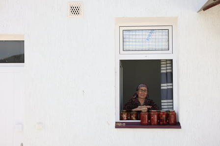 Person leaning out of a small window on a white wall, jars lined along the windowsill.