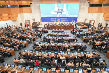 Crowded conference hall with a panel on stage and large screens.