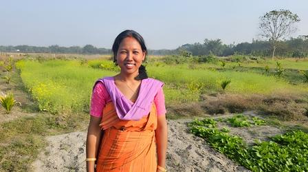 Woman with blurred face in purple top and orange dress stands in a sunny rural field.