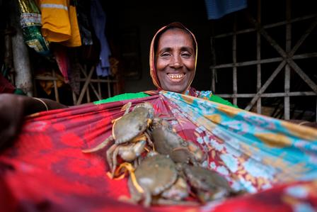 Photo of crabs clustered on a colorful cloth at a market stall; blurred figure in background.
