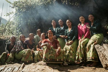 Group of people in traditional green-patterned clothing sitting on a rocky ledge outdoors, smiling.