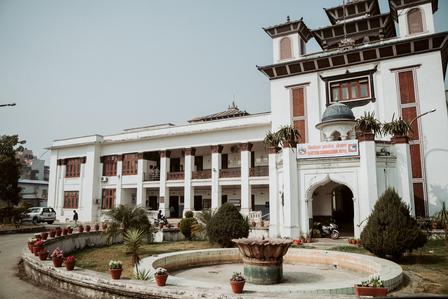 Grand white building with arches, a decorative gate, and a circular fountain in front.