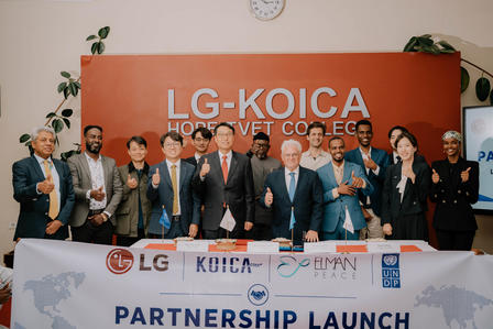 Group of professionals posing on stage during Partnership Launch with LG-KOICA banners.