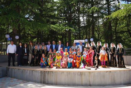 Group of people in colorful traditional and formal outfits posing on a circular outdoor stage.