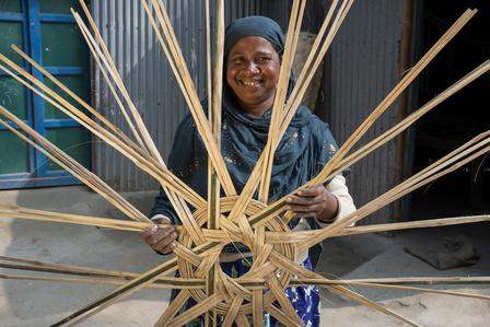 Photograph of a person weaving a large wooden sunburst wheel from spokes outdoors.