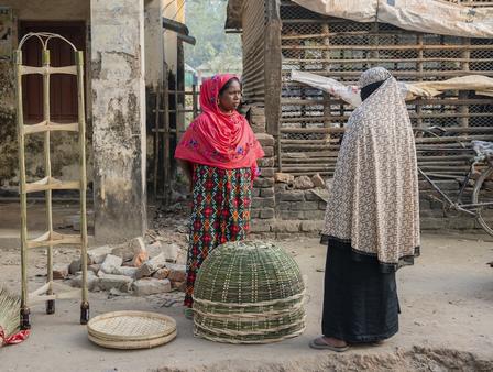 Photograph of two women in headscarves standing near a green domed basket outside a rustic building.