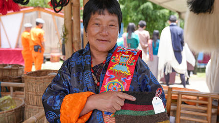 Person with blurred face wearing blue and orange traditional clothing at a colorful outdoor market.