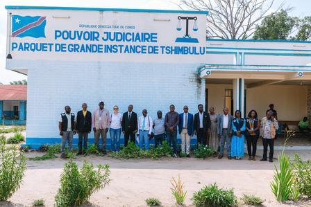 Group of people standing outside a blue and white judiciary building with a sign.