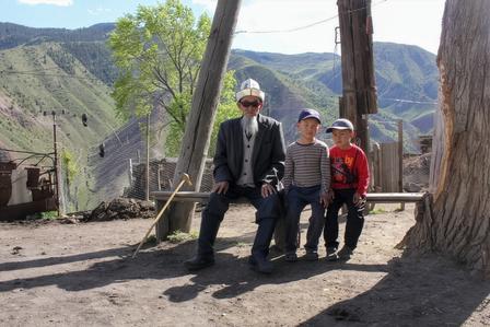 Three people stand near a wooden railing at a canyon overlook, mountains in distance.