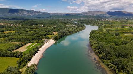 Aerial view of a winding river through a green valley with sandy banks and distant mountains.