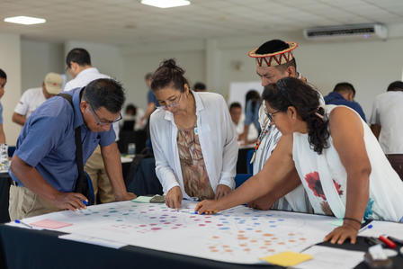 Photograph of people gathered around a large board covered with color stickers at a workshop.
