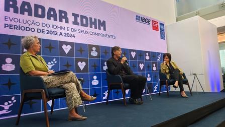 Panel discussion on stage with three speakers seated in chairs, blue backdrop featuring Radar IDHM.