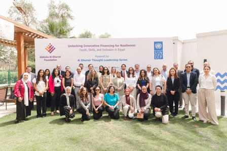 Large group of diverse people posing outdoors in front of a conference banner on a grassy lawn.