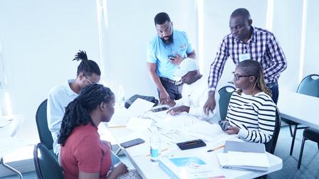 Diverse team collaborating around a bright table with papers and laptops in a sunny office.