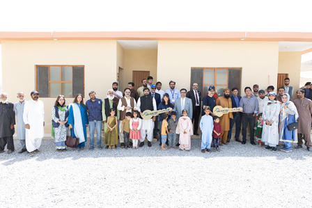 Photo of a diverse group posing outdoors in front of a light, single-story building.