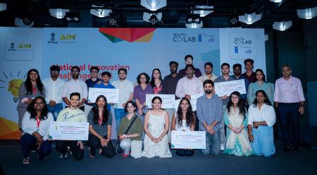 Diverse group posing on stage in front of a banner with logos at a conference.