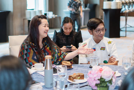Three people at a bright restaurant table, looking at a document, with pink flowers and desserts.