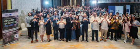 Large group posing for a conference hall group photo, banner visible on left.