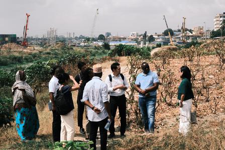 Group of people in casual clothing standing in a dry field with a distant city skyline and cranes.