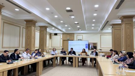 Large conference room with people around a long table; projection screen at the far end.