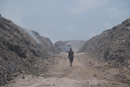 A lone motorcyclist rides along a dusty dirt road between tall, rocky canyon walls.