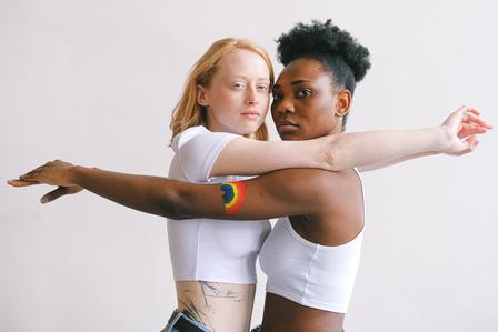 Photograph of two people hugging back-to-back in white outfits, faces blurred.