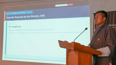 Photograph of a man at a podium delivering a slide presentation.