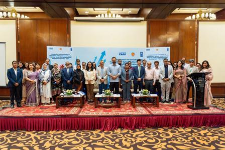 Group of professionals in formal attire posing on stage at a conference in a hotel ballroom.
