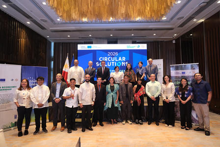 Photograph of a diverse group posing on a conference stage in front of a blue banner.