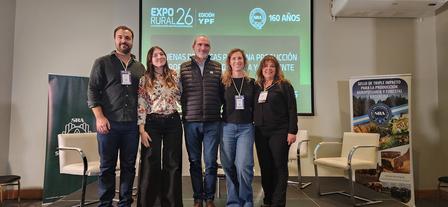 Six people stand on a stage for a conference photo, teal banner in the background.