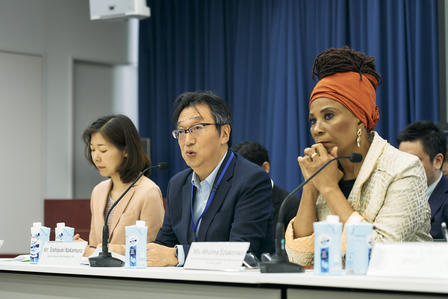 Panel of three diverse speakers at a conference table with water bottles and a blue curtain.