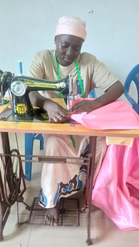 Older woman wearing a headscarf sewing pink fabric on a vintage treadle sewing machine.